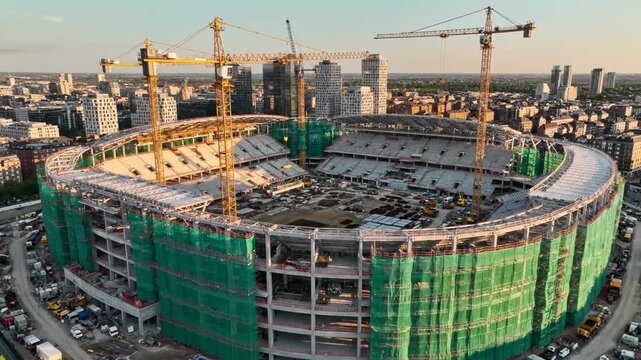 Large stadium under construction with cranes and scaffolding in urban setting
