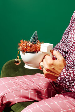 a man sits holding a mug decorated with a christmas tree and tinsel