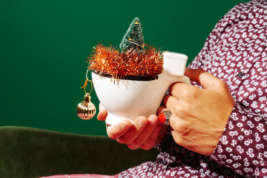 holding a toilet-shaped mug with tinsel and a tiny christmas tree