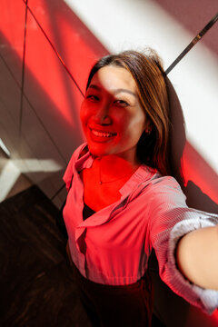 Smiling woman in red light takes a selfie.