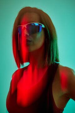 Stylish woman poses under vibrant lights wearing sunglasses