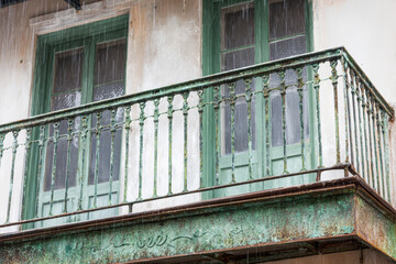 Old balcony during rain with weathered paint and green wooden doors in a historic building in a city