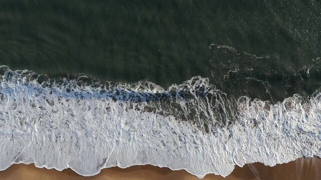 Aerial birdseye descendant over wave movement on beach during golden hour