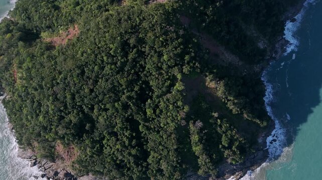 Aerial birdseye over green hill, tilt up revealing Barra do Sahy and Serra do Mar, Brazil