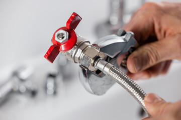 Plumber screws a flexible water pipe to a plumbing valve