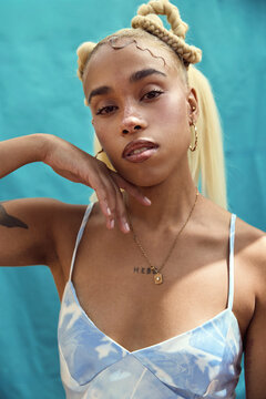 Front-facing portrait of woman with braided hair against teal backdrop