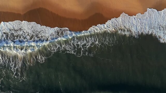 Aerial descendant over wave movement on beach during golden hour