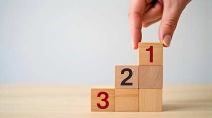 Wooden blocks numbered 1 2 and 3 arranged in a stair-like formation on a light wooden surface, with a hand placing the final block