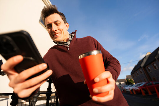 Gen Z Man Interacts With Phone Outside While Holding Coffee Cup