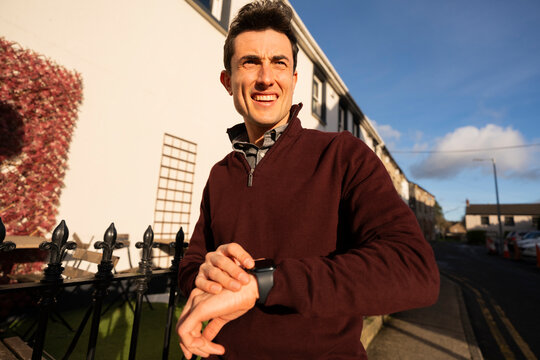 Gen Z Man Uses Smart Watch While Walking on Sidewalk Near House