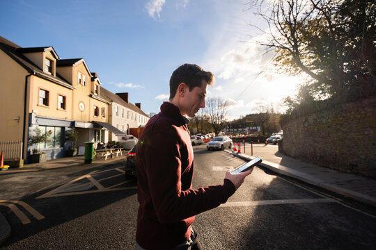 Man crosses the Street While Using Mobile Device in Small Town