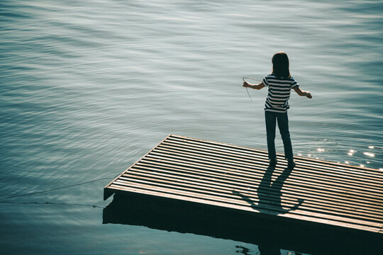 Child fishing from wooden dock near calm water