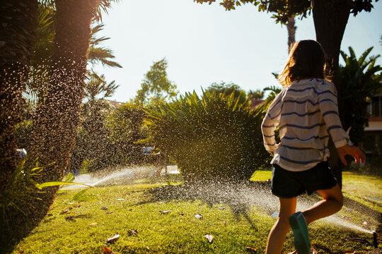 Child enjoys warm day running through sprinkler