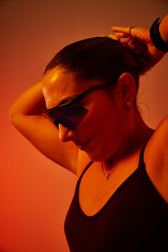 A woman ties her hair back in a sleek bun, wearing sporty sungla