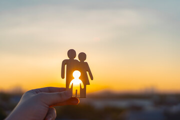 Family and fertility concept image showing a hand holding a wooden cutout of parents and child with sunlight background, symbolizing hope, parenthood, infertility, and desire to have children.
