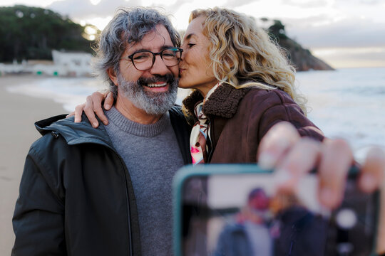 Couple sharing kiss while taking selfie on beach