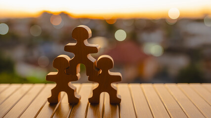 Teamwork and family support concept with wooden human figures forming pyramid shape on wooden table at sunset, symbolizing unity, collaboration, care, parenting, and strong relationship values.
