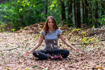 A woman is sitting on the ground with leaves flying around her. She is smiling and she is enjoying the moment