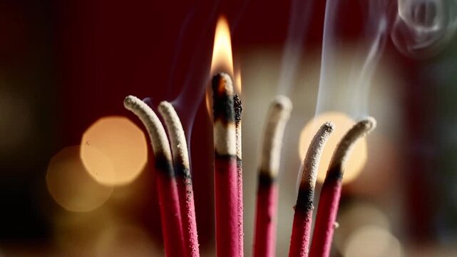 close up burning incense sticks with rising smoke in bokeh background