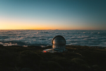Astronomical observatory on mountain peak above clouds at sunset