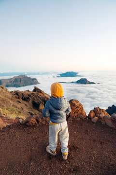 Toddler exploring mountain summit overlooking clouds