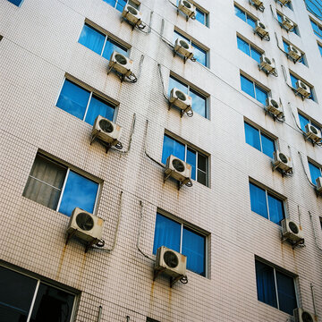 The tiled wall of an apartment building covered in AC units