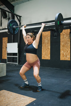 Pregnant woman practicing weightlifting a barbell in gym