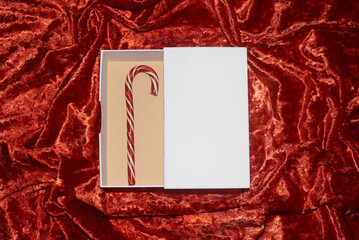 Candy cane placed in an open white gift box on soft red fabric