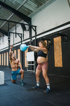 Pregnant woman training with kettlebell in gym with coach
