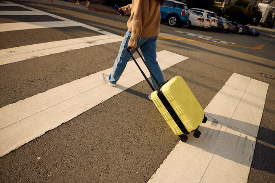Woman is crossing the street dragging a suitcase