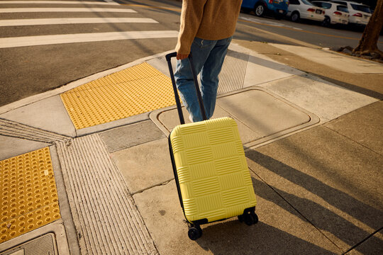 Woman walks across the street, pulling a suitcase behind her