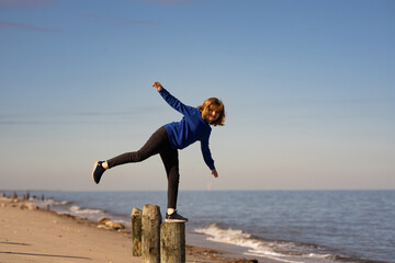 Child balances on wooden post. Childhood memories. Kid keeps balance outdoors. Young boy playing on calm sea. Cute boy walking on a balance beam. Happy childhood. Active child. Kids happiness.