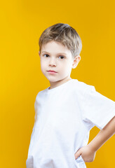 One Adorable Tranquil Little Male Kid Boy Of 5-6 Years Old Wearing White t-shirt Polo Isolated on Plain Yellow Background As Children Indoor Studio Portrait To Convey Childhood Lifestyle Concept