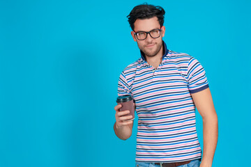 Smiling Good Loking Young Caucasian Handsome Brunet Man With Brown Paper Cup While Posing in Glasses Gesturing With Point Finger Against Blue