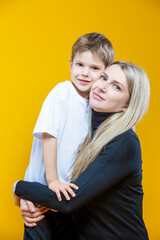 Smiling Cheerful Happy Couple Woman And Child Boy In Casual Clothing Having Mommy Little Kid Son Hug Cuddle While Posing on Yellow To Convey Mother's Love Day