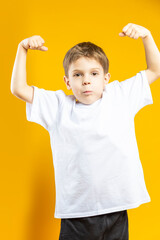 One Adorable Tranquil Little Male Kid Wearing White t-shirt Polo With Lifted Hands As Power Gesture Isolated on Plain Yellow Background As Children Indoor Studio Portrait To Convey Childhood Lifestyle