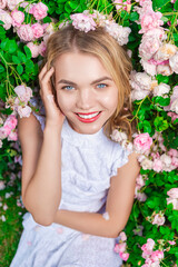 Closeup of Winsome Caucasian Fashion Blond Girl in Fragrant Pink Flowers Posing in White Dress on Grass in Summer Blossom Park as Fashion, Flowering, Gardening, Cosmetics Concepts.