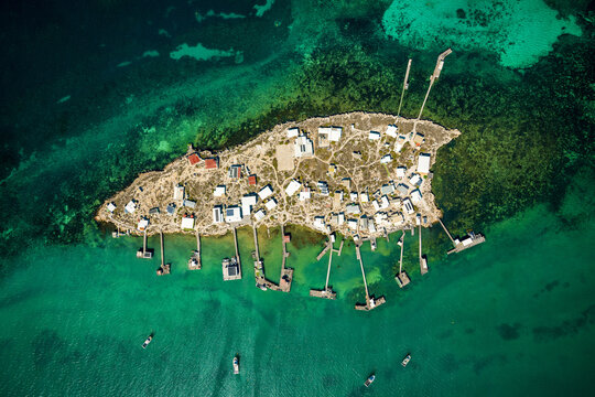 Remote island settlement with rows of shacks and jetties over turquoise water.
