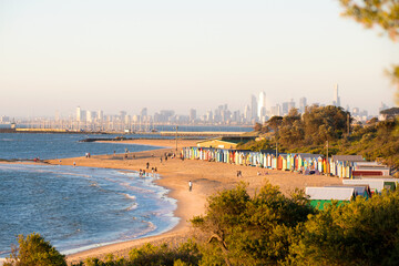 Brighton beach huts with the Melbourne skyline glowing in late-afternoon light.