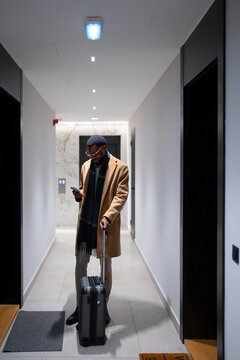Man with suitcase checks phone in a hotel hallway