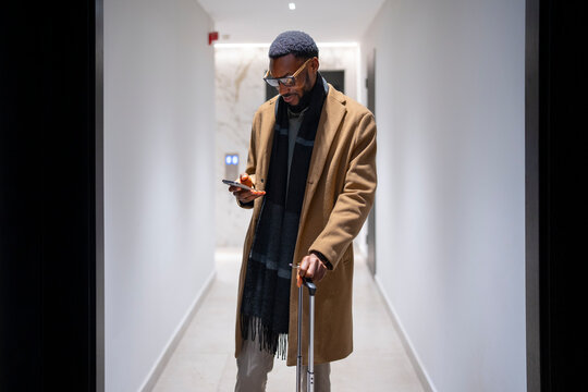 Man with suitcase checking phone in hotel hallway at night