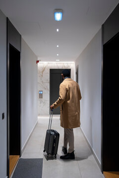 Traveler with suitcase walking down hotel hallway at night