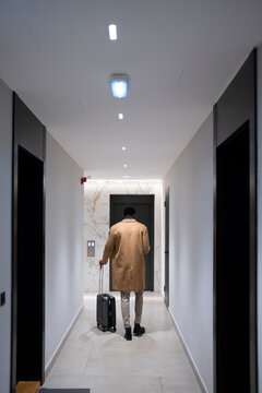 Traveling man walks down hotel corridor with luggage