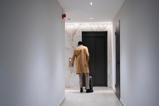 Man with suitcase preparing to enter elevator in hotel hallway
