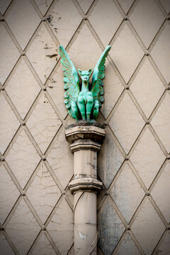 Weathered green-winged gargoyle perched on a cracked patterned fa&ccedil;ade
