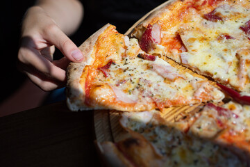 Pizza with melted cheese in hand. Pizza crispy crust. Pizza invites appetite with cheesy texture in hand. Slice of Pizza in hand, close up.