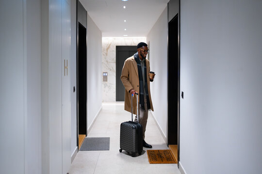Man with suitcase and coffee arriving at hotel elevator