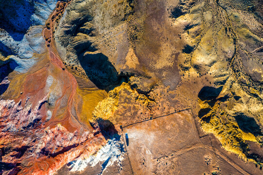 A lone vehicle beside vivid mineral bands carved into the desert.