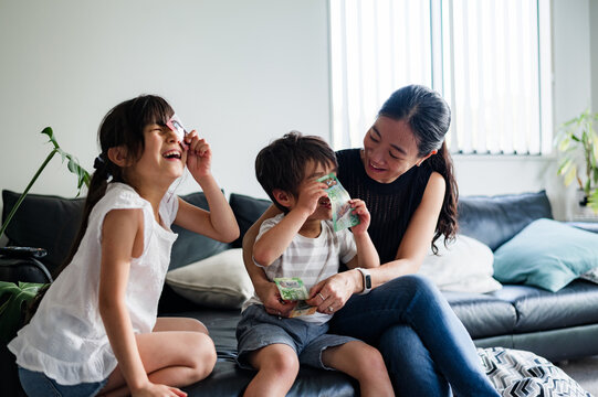 Two children enjoy a playful moment with their mother, laughing with money