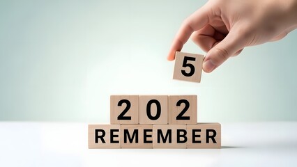 Hand placing a wooden block with the number 5 on top of a stack of blocks with the text 202 and remember